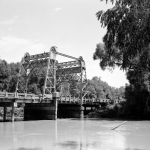 Lift bridge over river surrounded by large trees