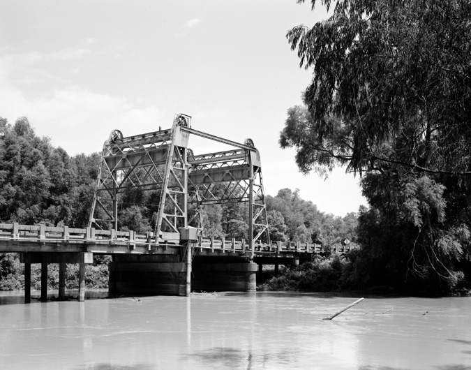 Lift bridge over river surrounded by large trees