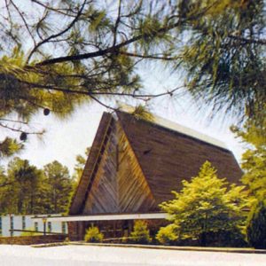 high wood building with framed pitched roof architectural features and cross surrounded by pine trees