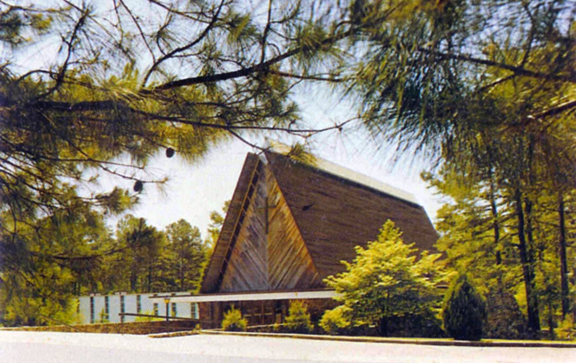 high wood building with framed pitched roof architectural features and cross surrounded by pine trees