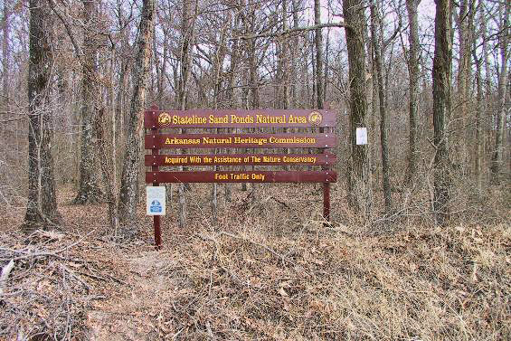 "State line Sand Ponds Natural Area Arkansas Natural Heritage Commission" sign in forest
