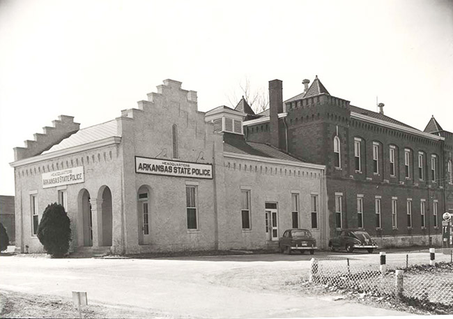 Long two-story building with single story addition with "Arkansas State Police" signs and arched entrance ways