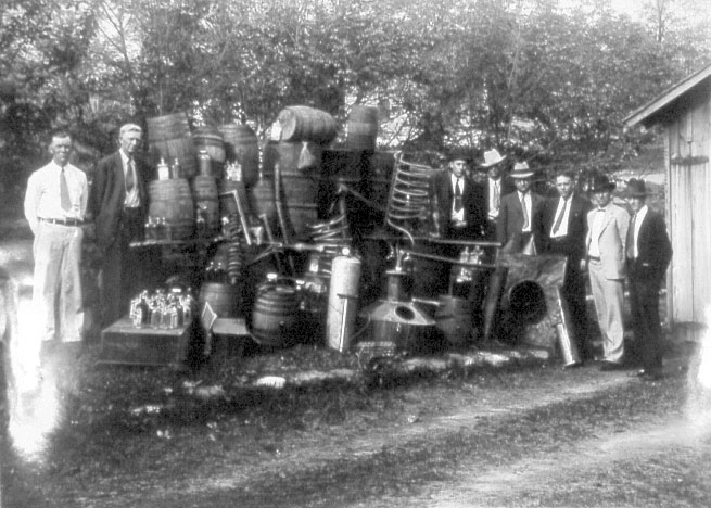White men in suits posing with large stills, barrels, and bottles