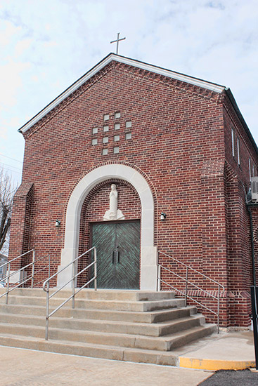 Multistory brick building with framed arch entrance and cross on its roof