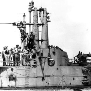 Navy men on submarine deck with U.S. flag and artillery