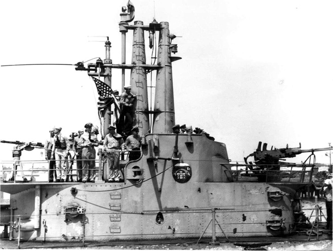 Navy men on submarine deck with U.S. flag and artillery