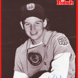 Young white woman in baseball uniform with cap and glove inside red border with text and shield logo signed "Sue Kidd"