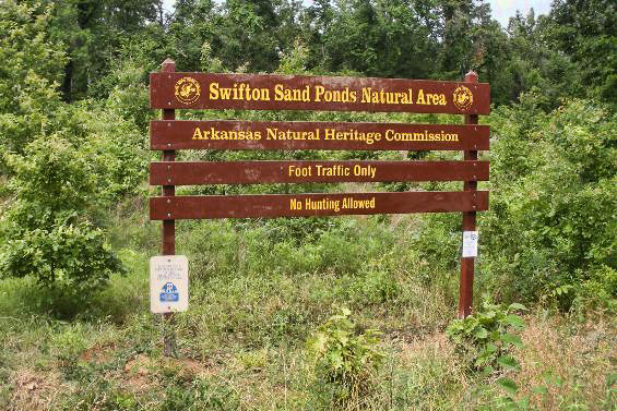 "Swifton Sand Ponds Natural Area Arkansas Natural Heritage Commission" sign with trees behind it