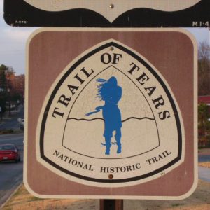 Street sign with triangular logo labeled "Trail of Tears National Historic Trail" featuring Native American man in its center in blue