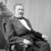 white man with mustache in suit sitting on chair