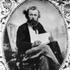 Portrait white man with beard and book seated by tents in ornate metallic frame
