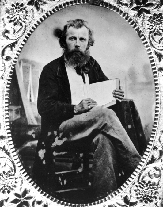 Portrait white man with beard and book seated by tents in ornate metallic frame