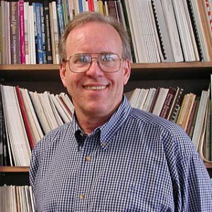 white man in glasses in front of bookshelves