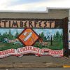 "Timberfest" lumberjack mural with crossed ax and saw sign and business logos on the side of a brick building