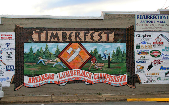 "Timberfest" lumberjack mural with crossed ax and saw sign and business logos on the side of a brick building