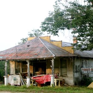 Abandoned and dilapidated building with junk on covered porch and tree on its right side