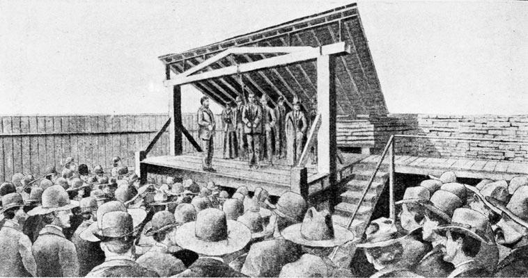 Crowd of people gathered around a gallows where white men in suits are hanging a man