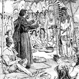 White man in robes holding a cross talking to a group of Native Americans