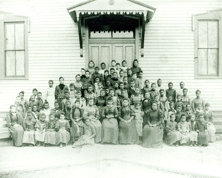 Group of African-American children and teachers outside a clapboard school house