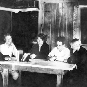Group of white students sitting around a wooden table in a bare room
