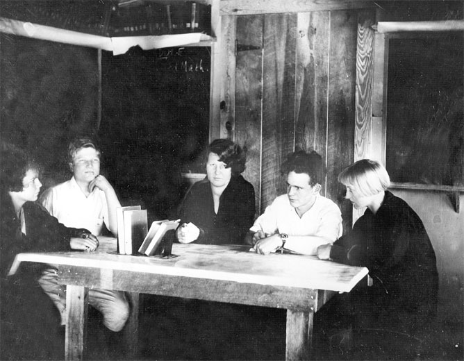 Group of white students sitting around a wooden table in a bare room