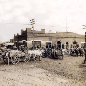 Group of people with horse-drawn buggies parked outside a store in Rogers
