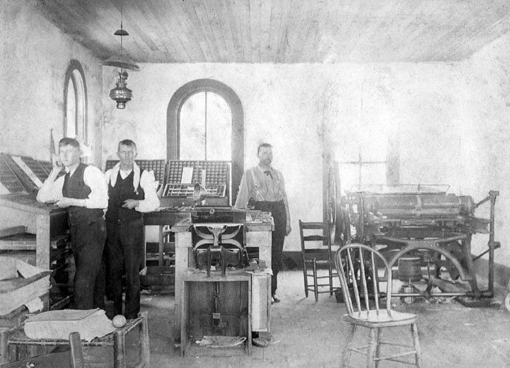 Three white men at work in a printing room with arched windows