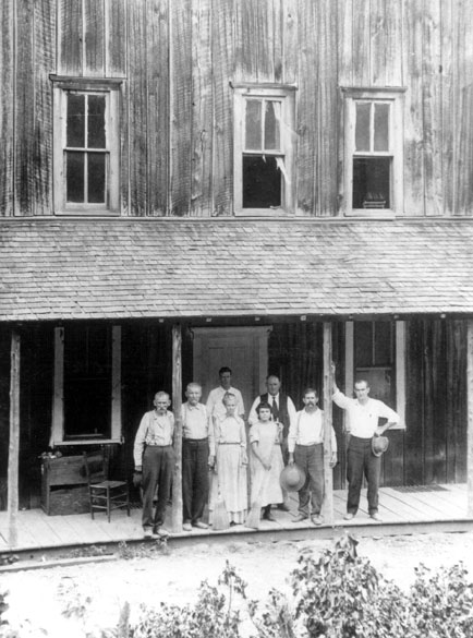 Group of white men and women pose in front of two story building