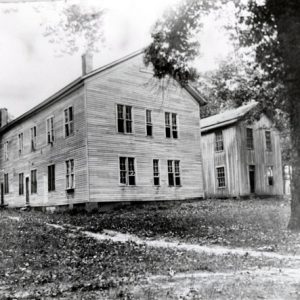Two large two story wood frame buildings among trees dirt path in foreground