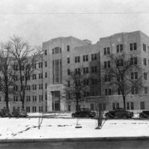 multistory brick building with bare trees on snow covered grounds and cars parked alongside