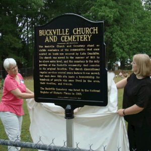 Older white women revealing "Buckville Church and Cemetery" sign