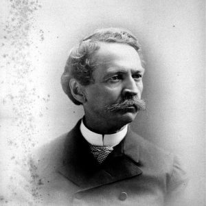 White man with curly hair and mustache in suit and white collar