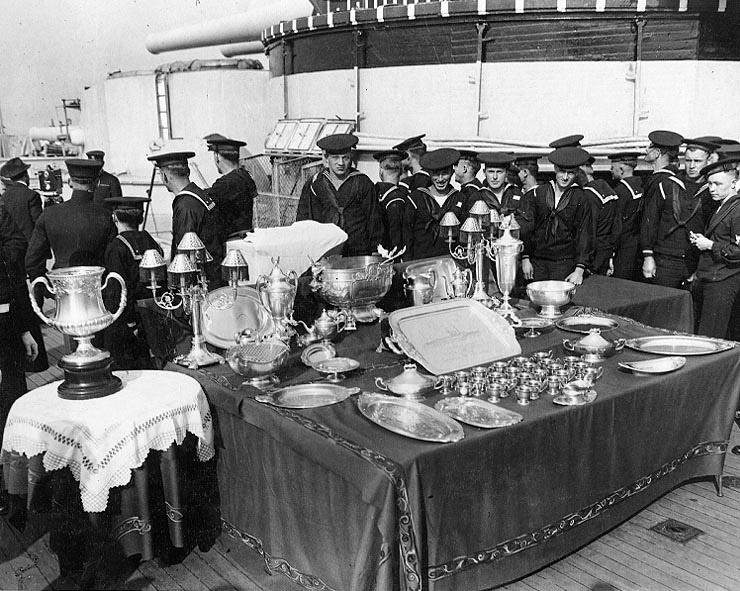 naval crewmen on deck of ship looking at silver trays, bowls, and cups