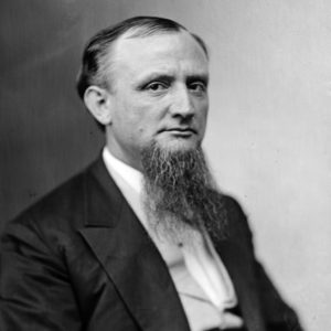 White man with beard sitting in suit and vest