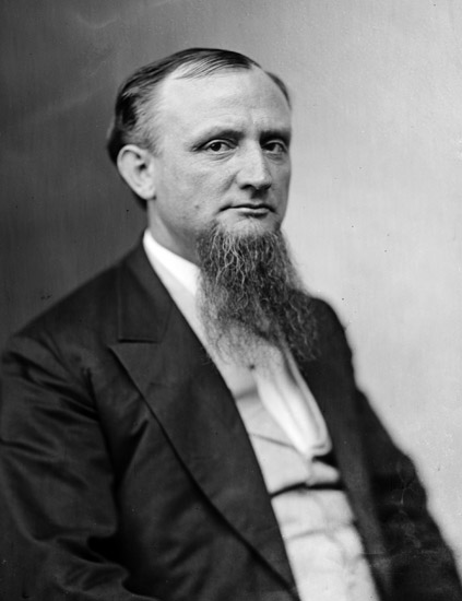 White man with beard sitting in suit and vest