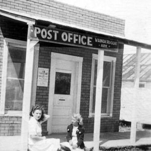 young white woman and blond girl sitting on the platform in front of a small brick building with a white door