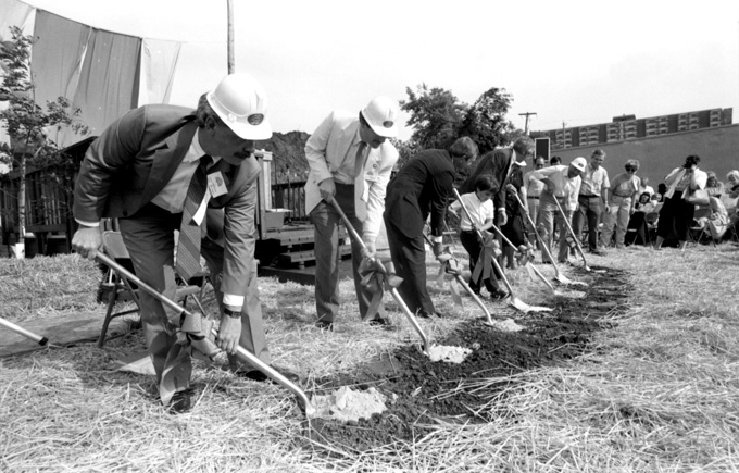 Groundbreaking ceremony including white men and child holding shovels with audience