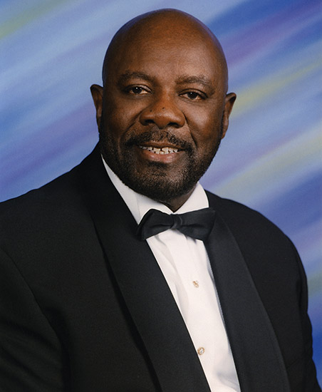 African-American man with mustache and beard smiling in tuxedo