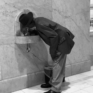 African-American man in suit and hat drinking from fountain labeled "colored"