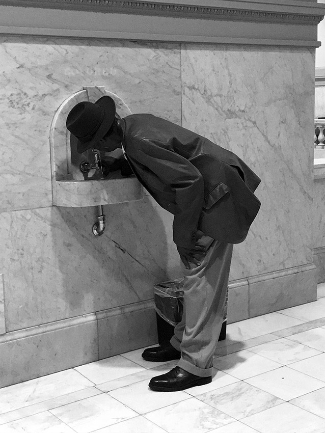 African-American man in suit and hat drinking from fountain labeled "colored"