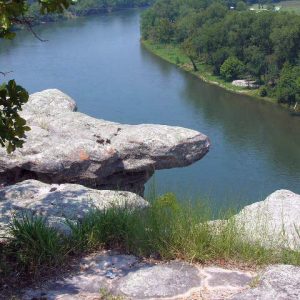 River view from rocky cliff with trees, grass, and house in distant field