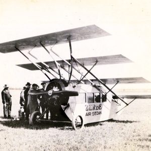 White men stand in field outside four-winged, propeller-driven vehicle labeled "Zerbe Air Sedan"
