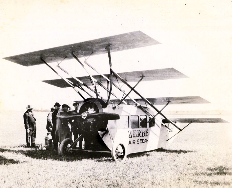 White men stand in field outside four-winged, propeller-driven vehicle labeled "Zerbe Air Sedan"