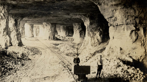 Interior expansive mine earth columns two white male figures foreground cart on tracks