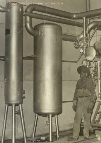 man in welding mask stands in front of large metal cylinders