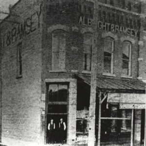 Two white men standing in doorway of large two story brick building