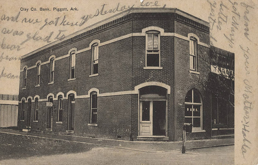 Postcard showing Two story brick building with corner entrance and arched windows; card has writing on it in pencil