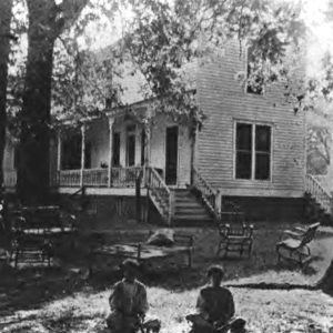 Children sitting on lawn in front of two story wooden house