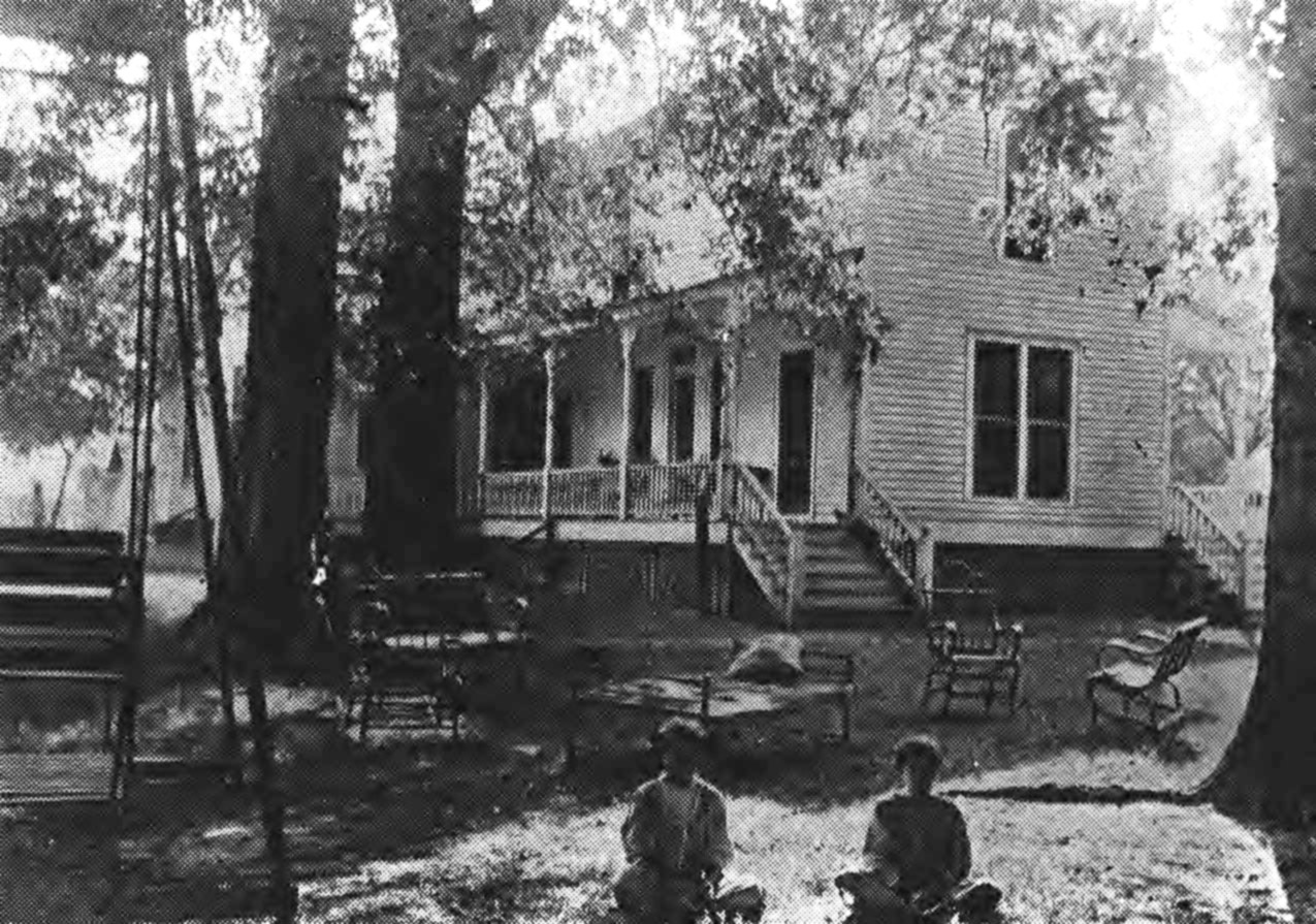 Children sitting on lawn in front of two story wooden house