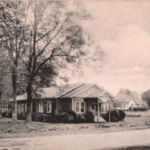 Single story building with front porch amid tall trees